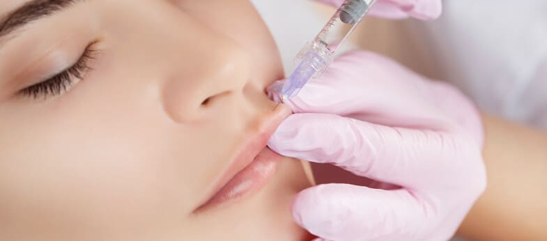 botox wimbledon - A woman is receiving a lip enhancement injection at the Ridgway Dental skin clinic in Wimbledon. The procedure, performed by a professional wearing pink gloves, ensures a safe and sterile environment. The treatment focuses on enhancing the woman's lips, contributing to a fuller and more youthful appearance. The woman's face shows a serene expression, reflecting the expertise and care provided by the clinic's staff.